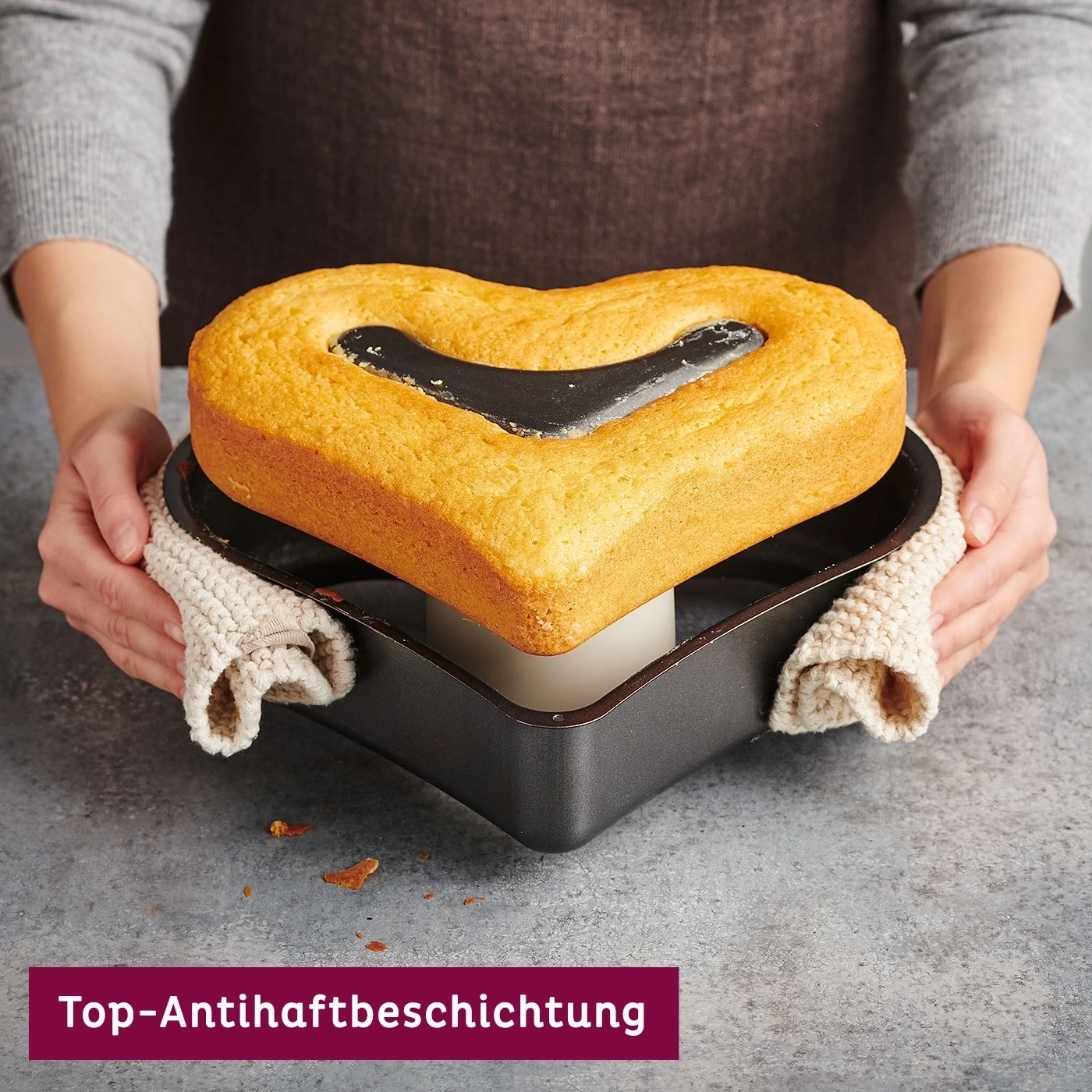Herzförmiger Kuchen in Backform, gehalten von Person mit Topfhandschuhen