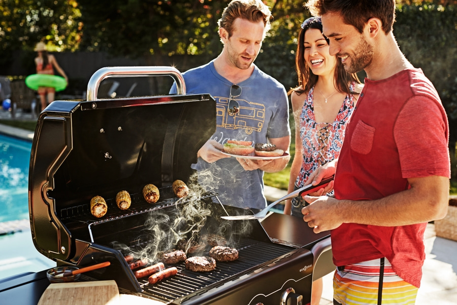 Grillen im Garten mit Freunden. Burger, Würstchen und Maiskolben auf dem Grill.