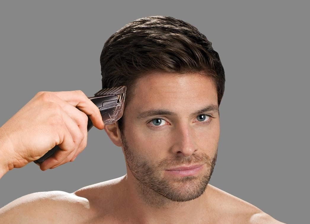 Mann schneidet sich die Haare mit einem Haarschneider vor grauem Hintergrund