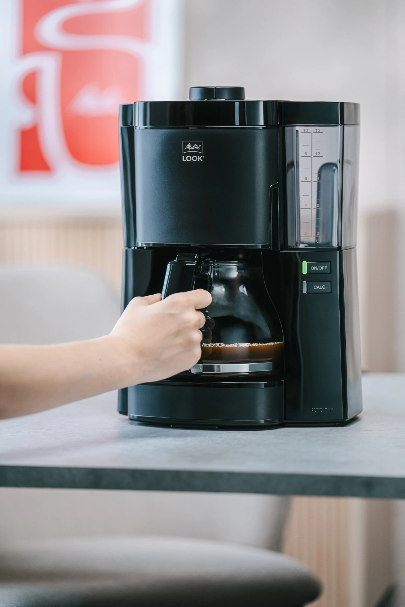 Eine Person nimmt eine Kaffeekanne aus einer schwarzen Kaffeemaschine.