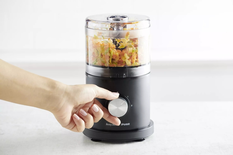 Eine Person, die einen schwarzen Küchenmixer bedient, der Gemüse zerkleinert.