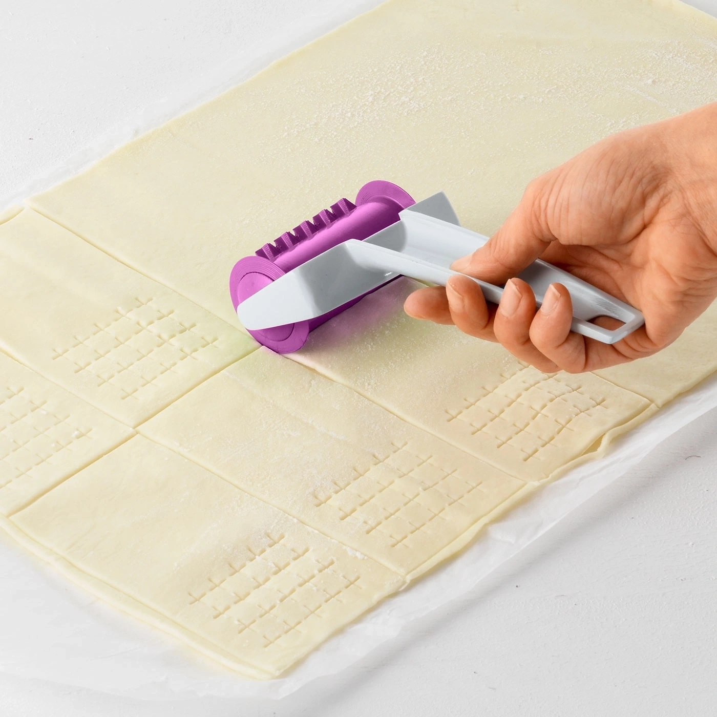 Hand mit Teigroller schneidet Teig in Quadrate, Backen, Küche, Werkzeug
