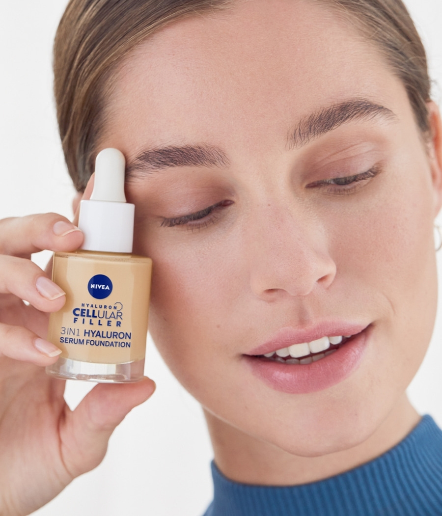 Frau hält Nivea Cellular Filler Serum Foundation in der Hand, lächelt.
