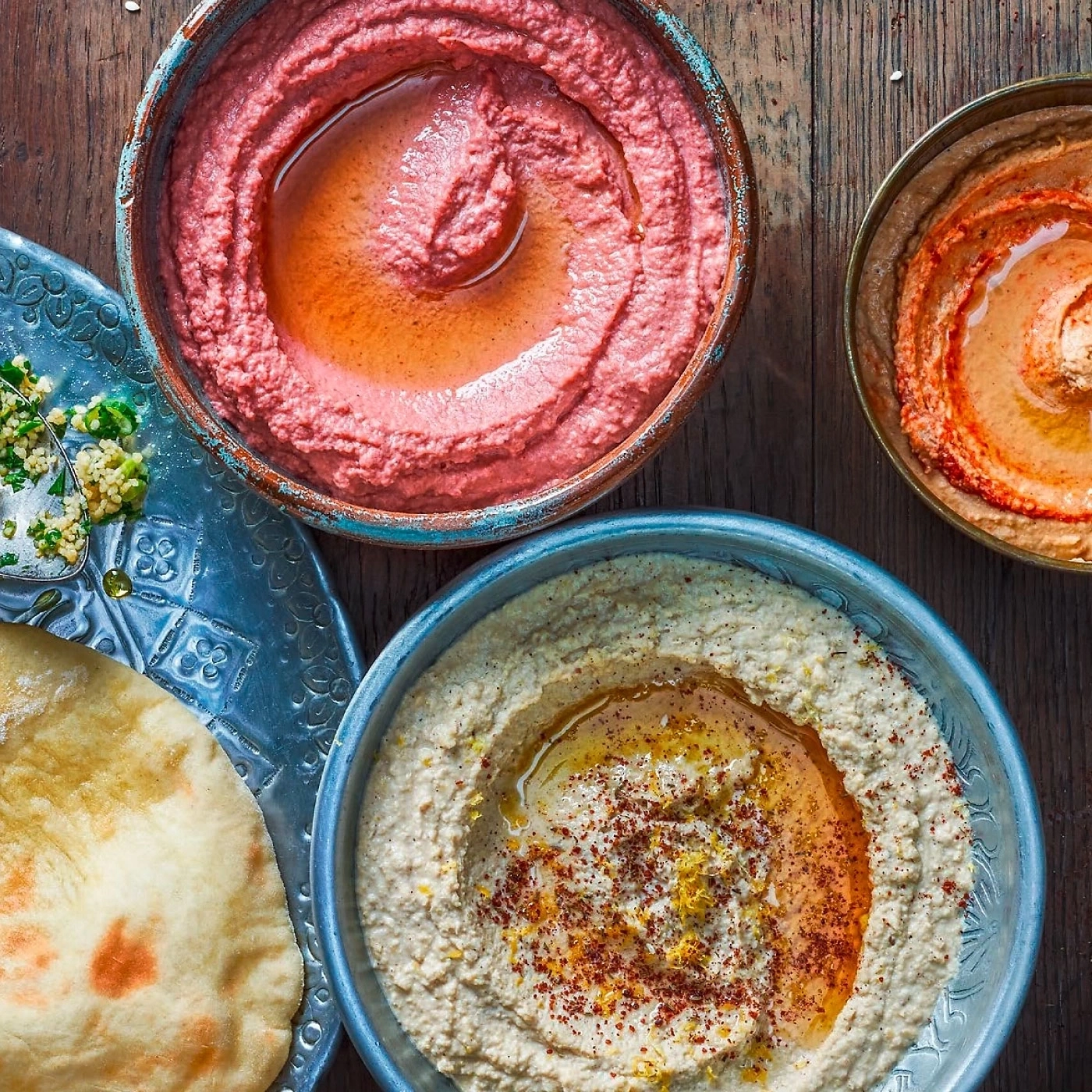 Hummus-Gerichte mit Brot und Beilagen auf einem Holztisch