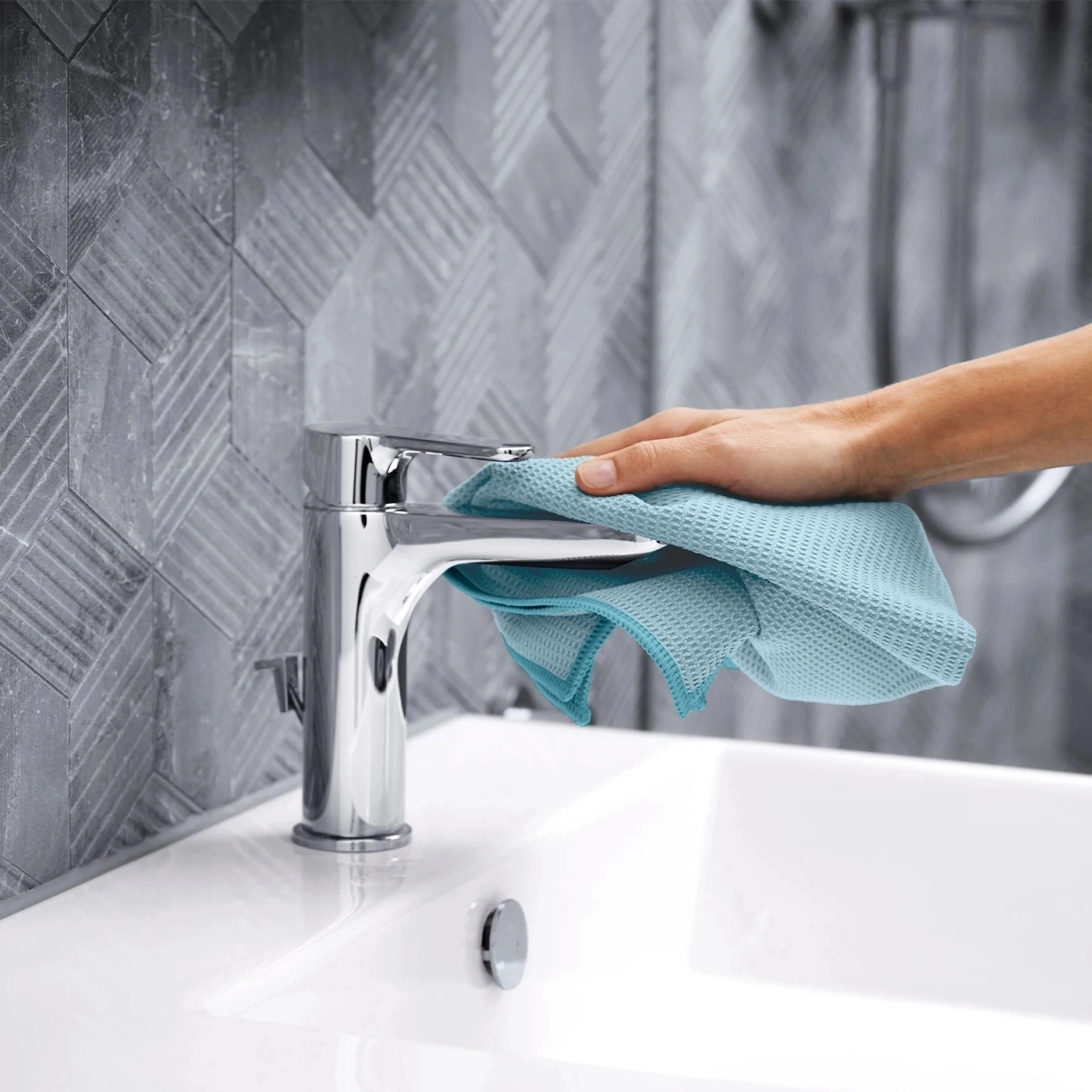 Person reinigt Wasserhahn mit blauem Tuch im Badezimmer, Nahaufnahme