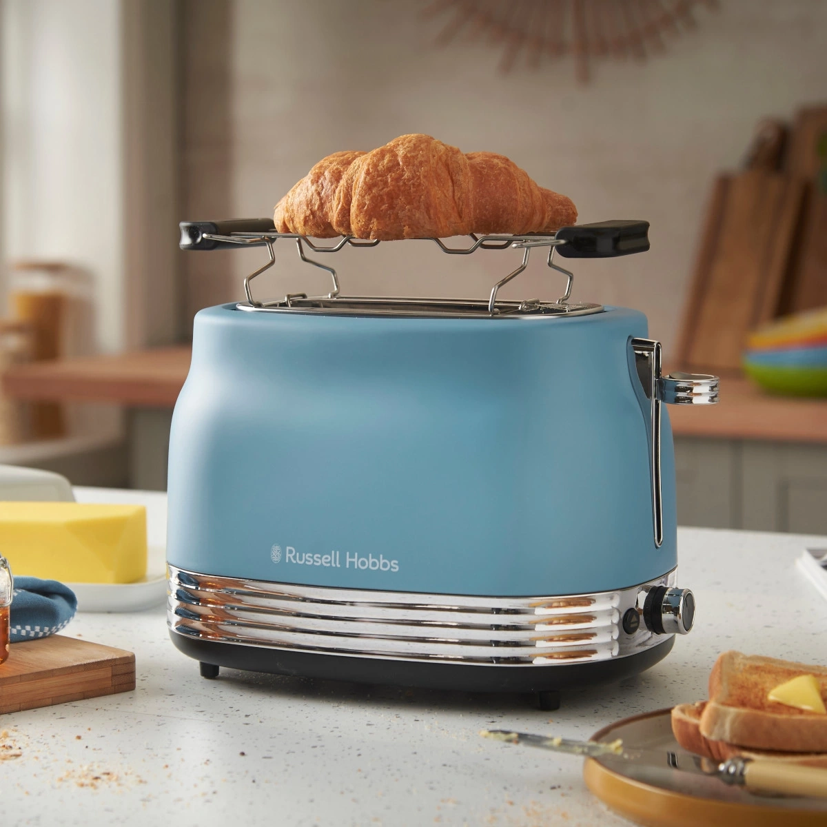 Ein blauer Russell Hobbs Toaster mit einem Croissant und Toast im Hintergrund