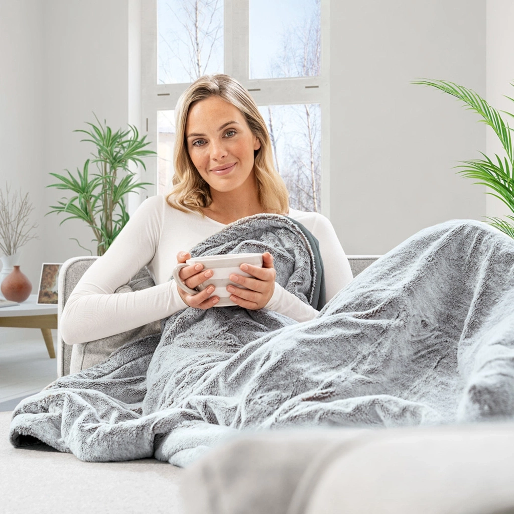 Frau mit Tasse unter Decke auf Sofa