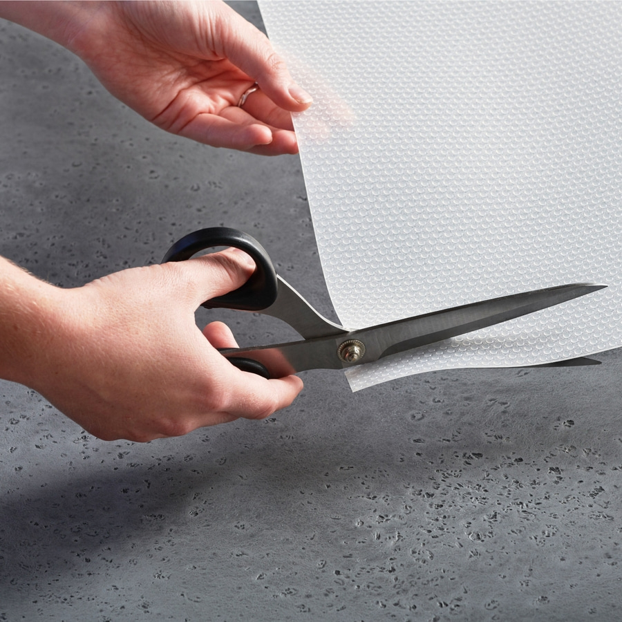 Person schneidet mit einer Schere ein weißes Blatt Papier auf grauem Untergrund.