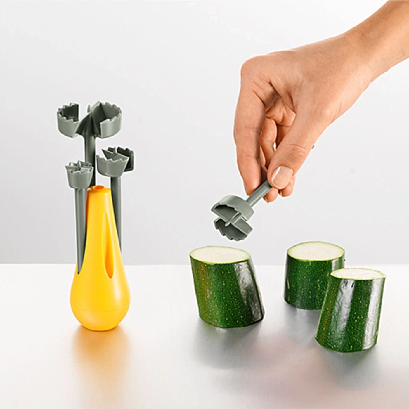 Person hält Werkzeug über Zucchini. Gelbes Objekt und graue Werkzeuge.