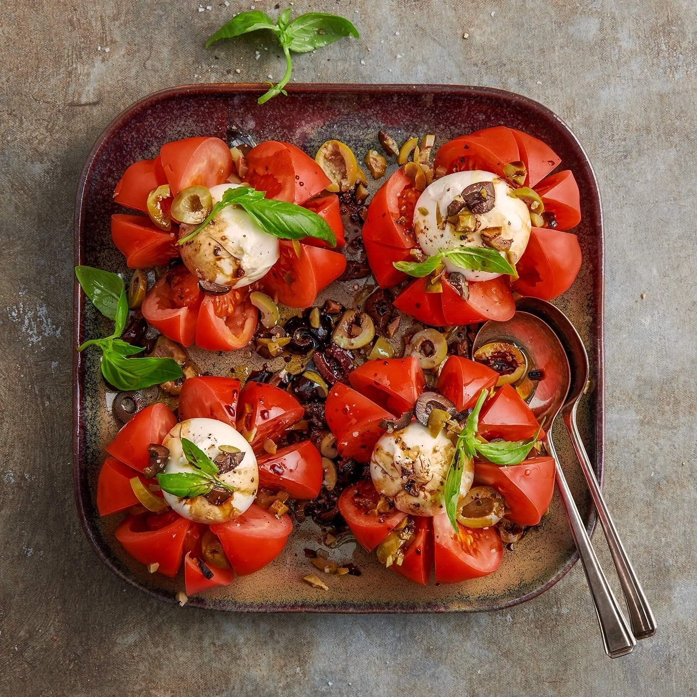 Tomaten-Mozzarella-Salat auf einem Teller mit Oliven und Basilikum