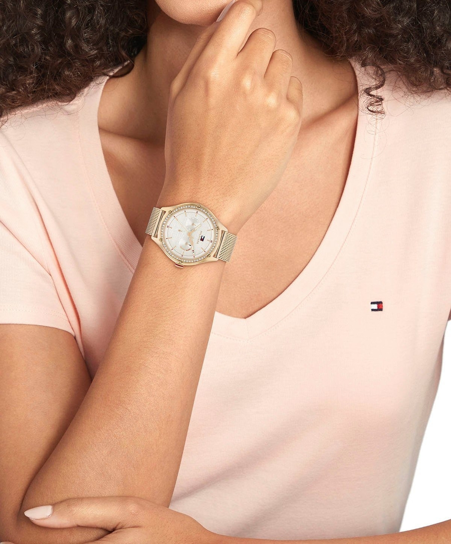 Frau mit goldener Uhr und rosa T-Shirt, Tommy Hilfiger Logo.