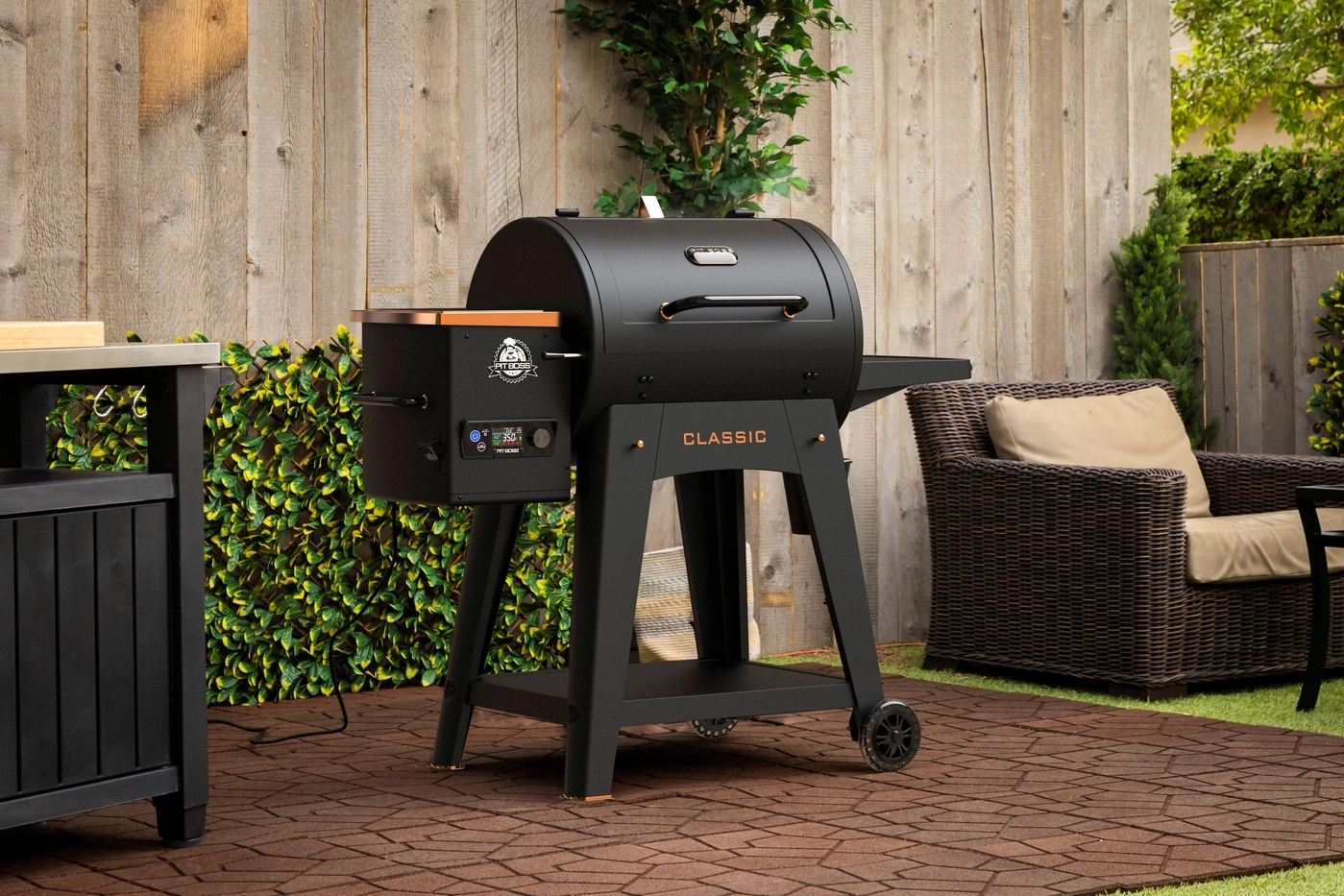 Ein schwarzer Pit Boss Grill steht auf einer Terrasse neben einem Sessel.