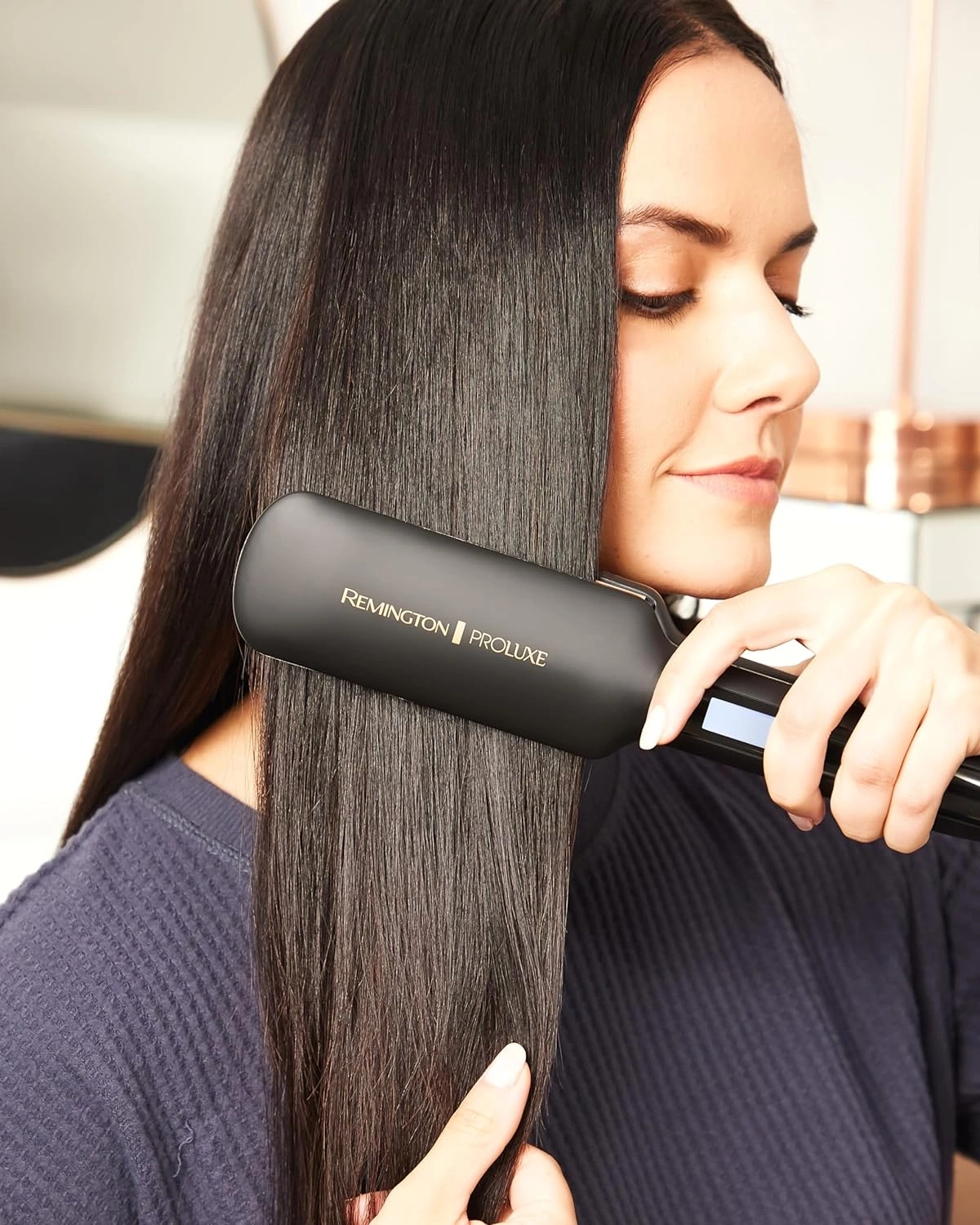 Frau glättet ihre Haare mit einem Remington Proluxe Glätteisen. Schwarze Haare.