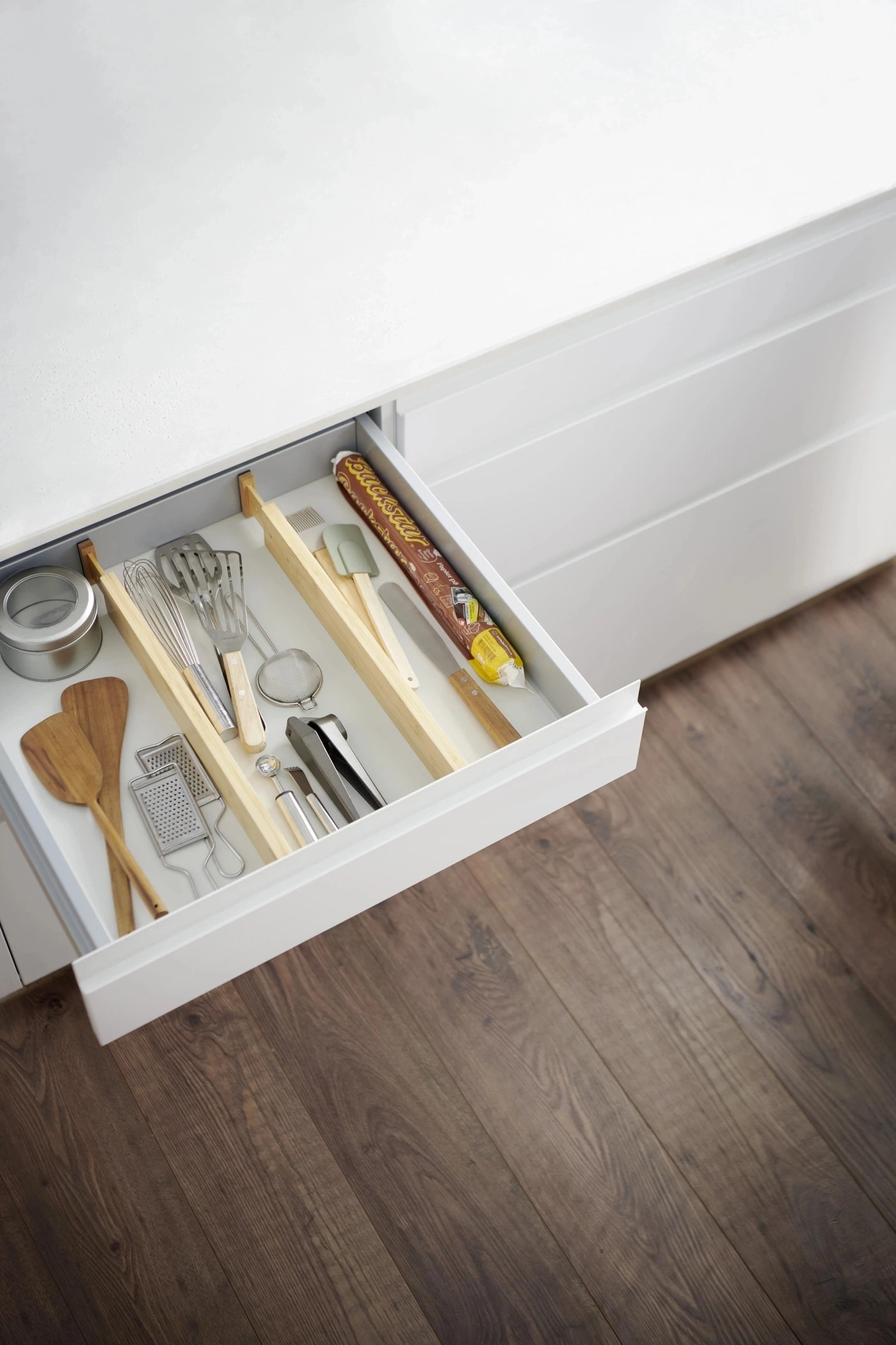 Küchenschublade mit Kochutensilien, Holzspateln, Schneebesen und Reibe.
