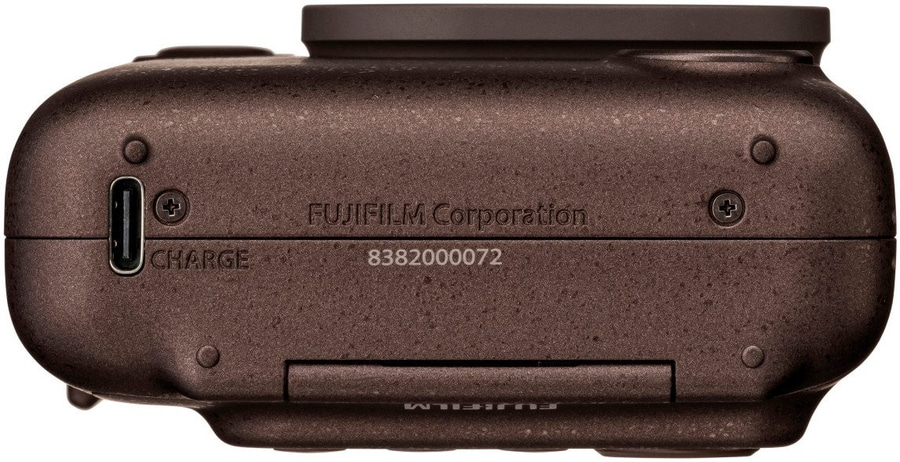 Die Unterseite einer braunen Fujifilm-Kamera mit Ladeanschluss und Seriennummer