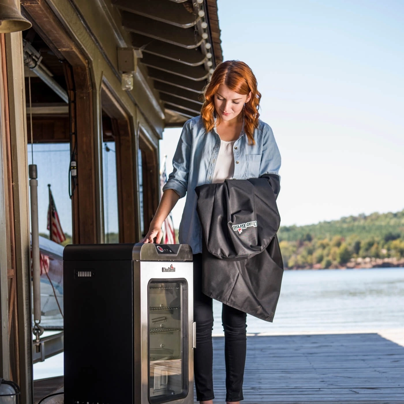 Frau mit Grill und Abdeckung am Seeufer, sonniger Tag