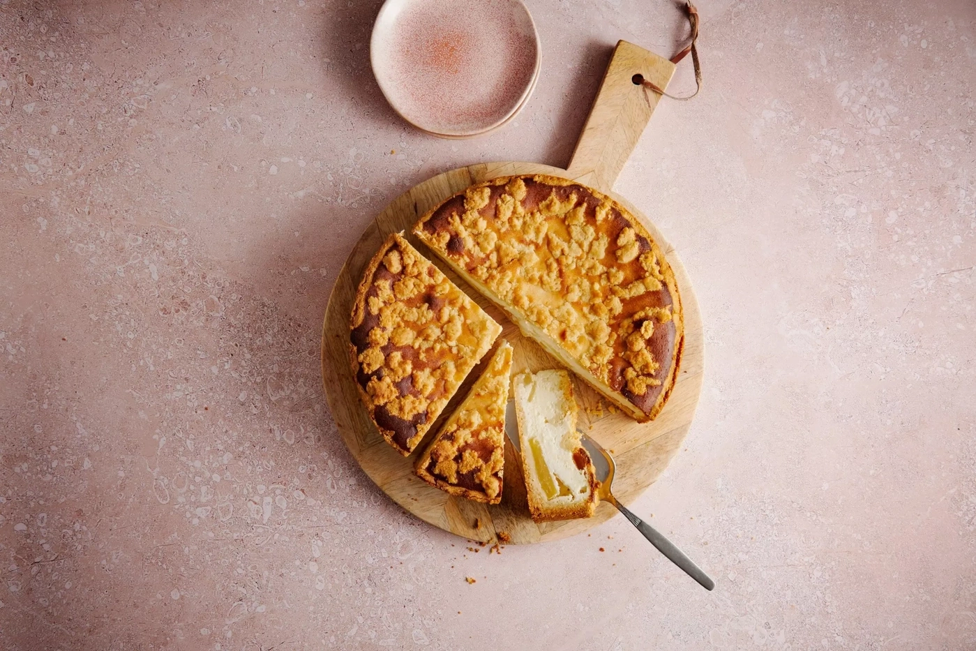 Ein angeschnittener Käsekuchen mit Streuseln auf einem Holzbrett mit einem Messer.