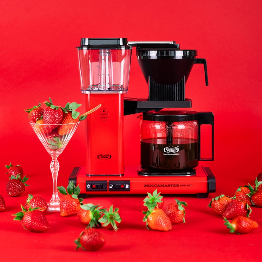 Rote Kaffeemaschine mit Erdbeeren. Moccamaster Select. Roter Hintergrund. Glas mit Erdbeeren.
