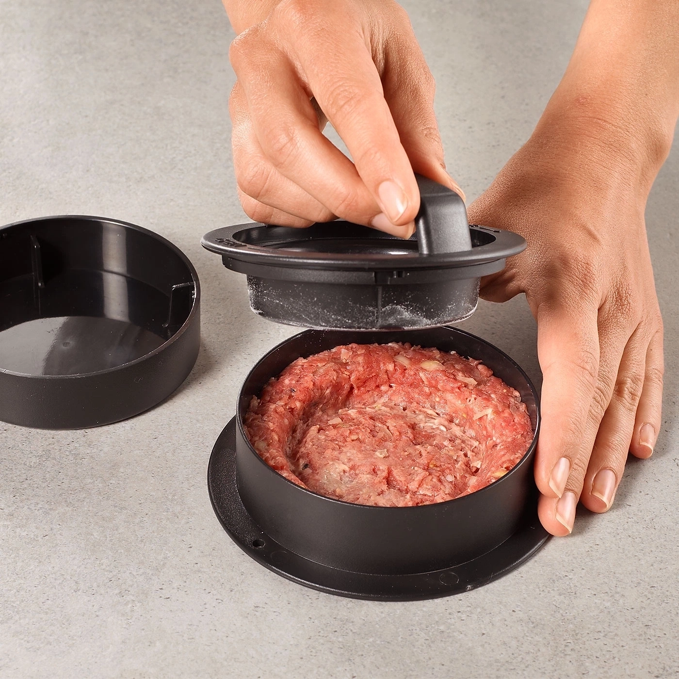 Person formt Burger mit Burgerpresse auf grauem Untergrund