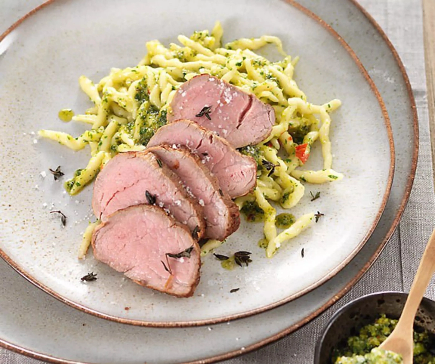 Geschnittenes Schweinefilet mit grüner Soße und Pasta auf Teller