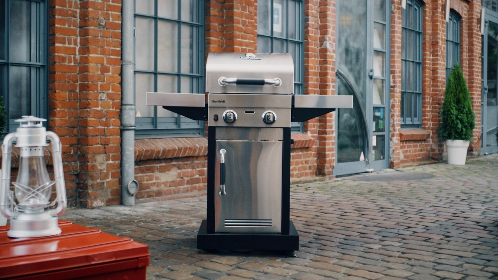 Ein Gasgrill steht auf einem Kopfsteinpflaster vor einem Backsteingebäude.
