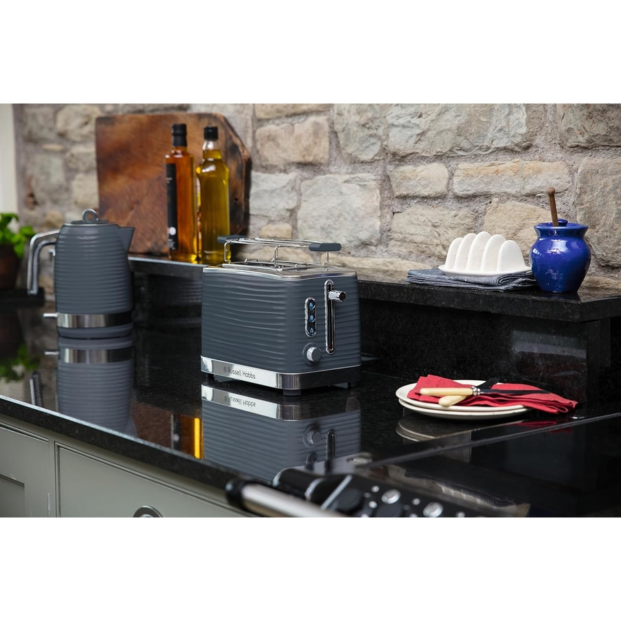 Grauer Toaster, Wasserkocher, Ölflaschen, Teller mit Besteck, Küche, Steinwand.