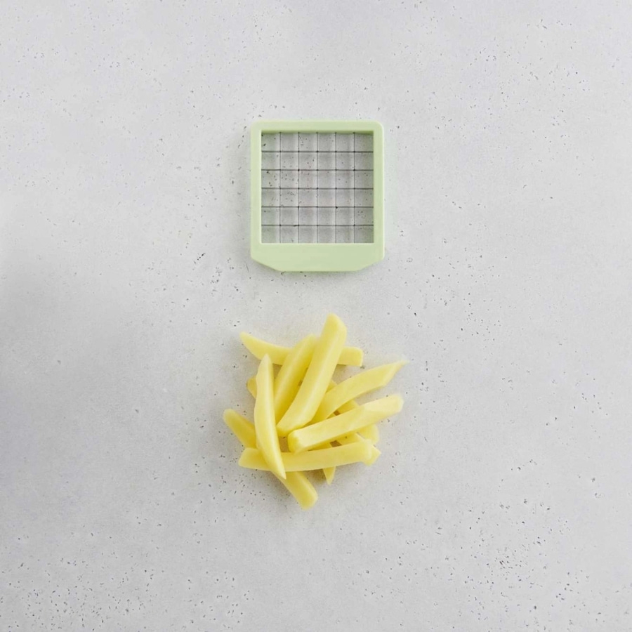 Pommes Frites und ein grüner Pommesschneider auf grauem Hintergrund