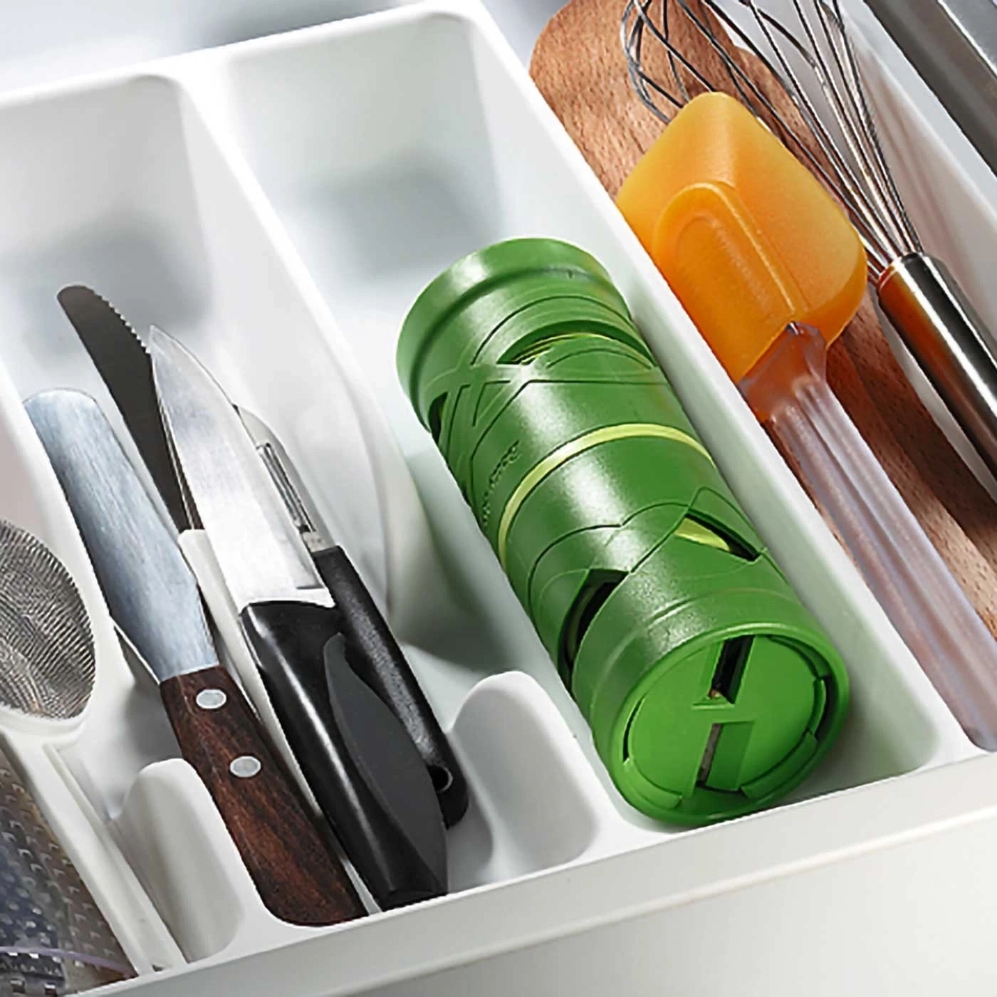 Küchenutensilien in einer Schublade: Messer, Schneebesen, Spatel, grüner Behälter.
