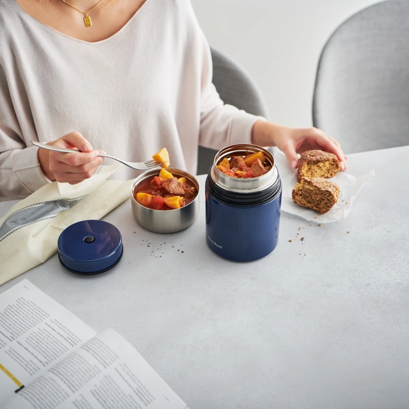 Person isst Eintopf mit Brot, daneben eine Thermoskanne und ein Magazin.