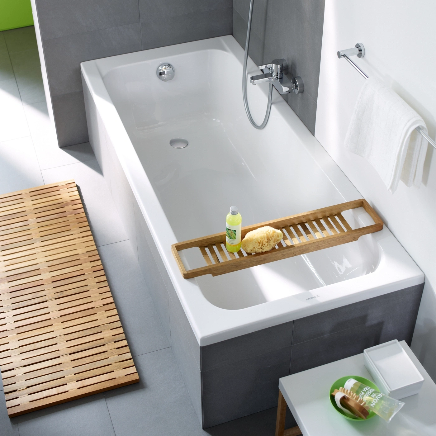 Badezimmer mit Badewanne, Holzmatte, Seife, Schwamm und Handtuchhalter