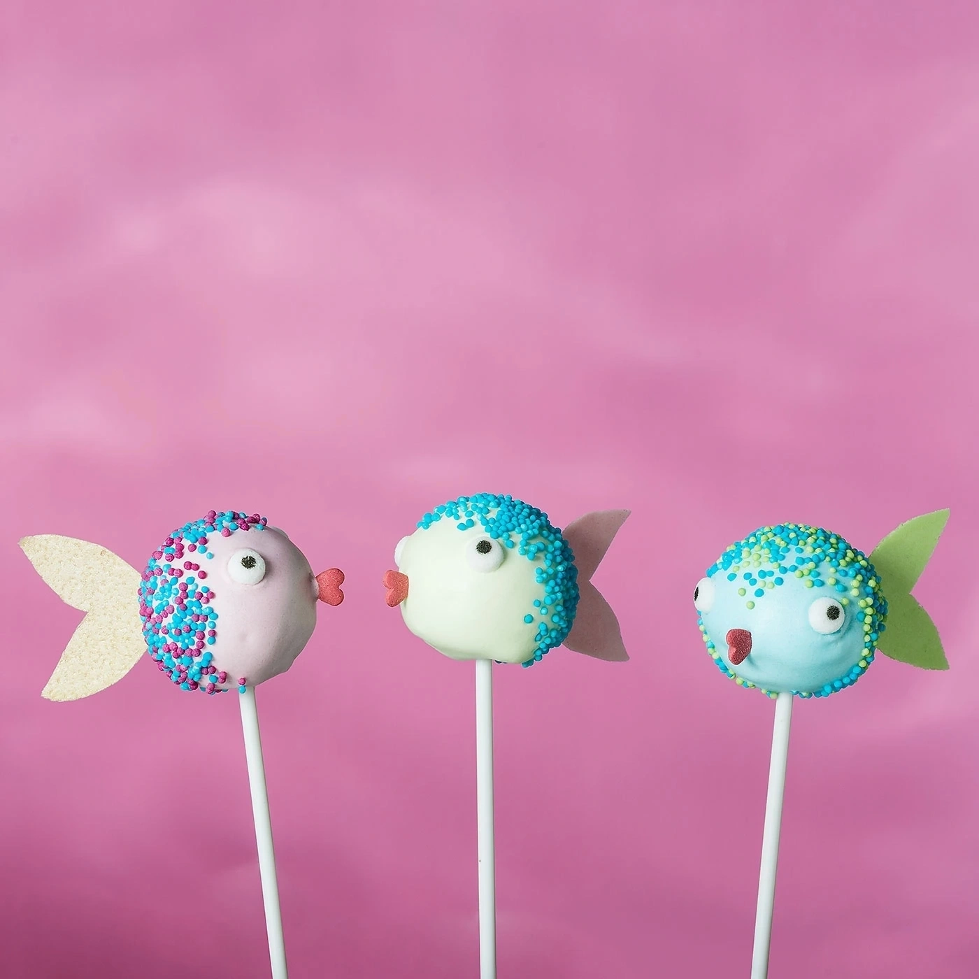 Drei Fisch-Lutscher vor pinkfarbenem Hintergrund. Süße, dekorierte Kuchen am Stiel.