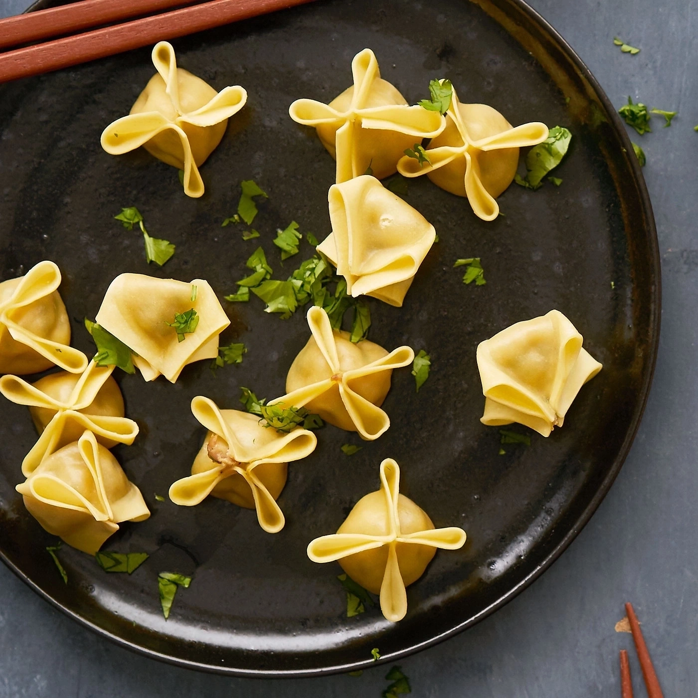 Teller mit Ravioli, Petersilie und Stäbchen auf grauem Hintergrund