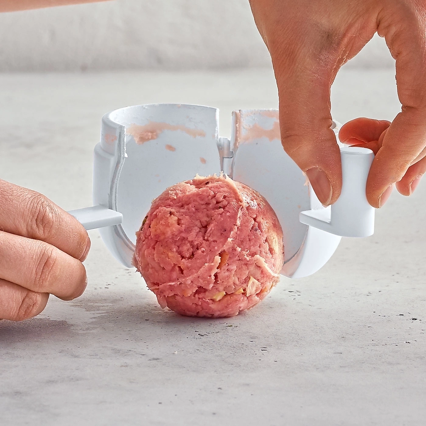 Person formt Fleischbällchen mit einem Werkzeug. Nahaufnahme der Hände und des Fleischs.