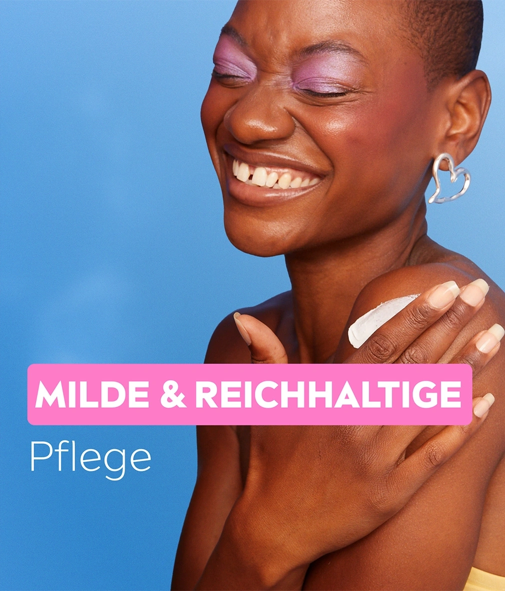 Eine Frau mit lila Lidschatten und Herz-Ohrring lächelt, mit der Aufschrift "Milde & Reichhaltige Pflege".