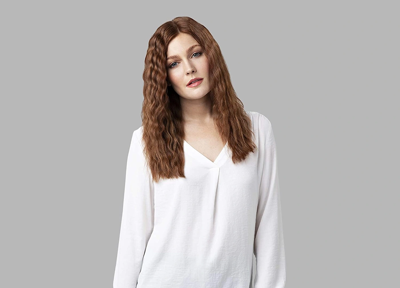 Eine Frau mit roten Locken und einem weißen Hemd vor grauem Hintergrund