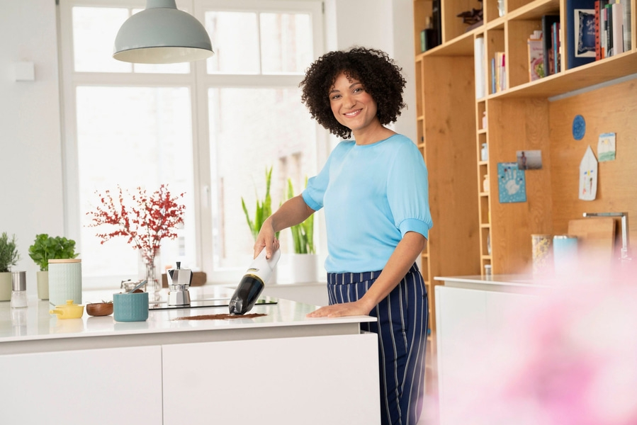 Frau saugt Kaffeepulver in der Küche mit einem Handstaubsauger auf.