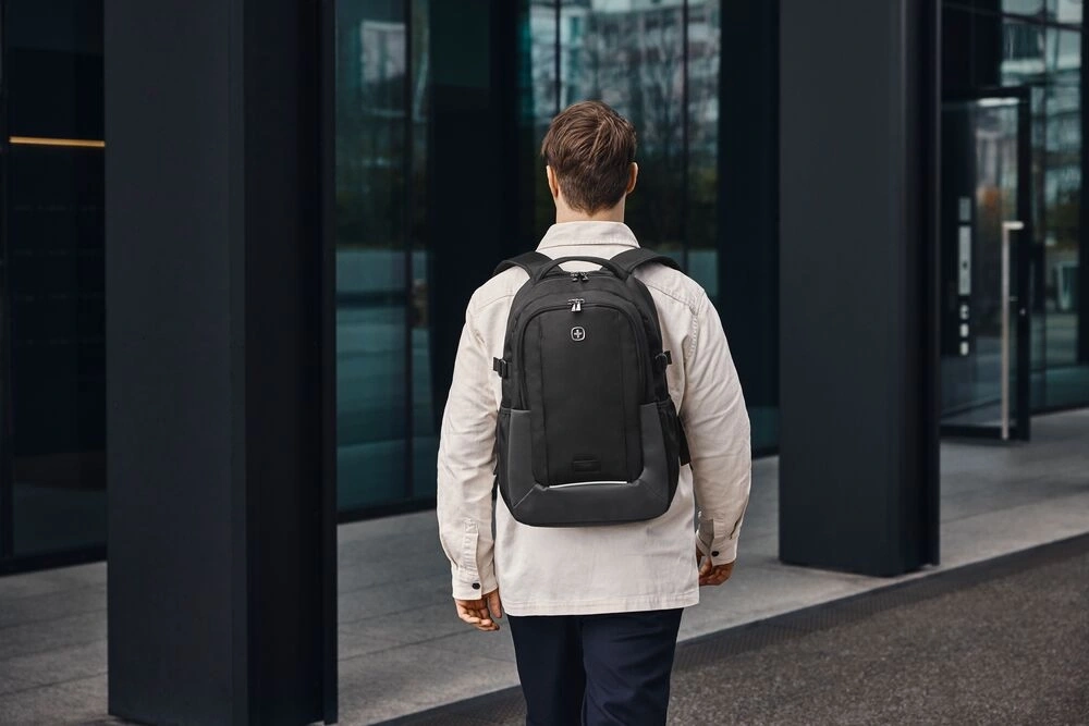Mann mit schwarzem Rucksack geht vor einem Gebäude entlang.