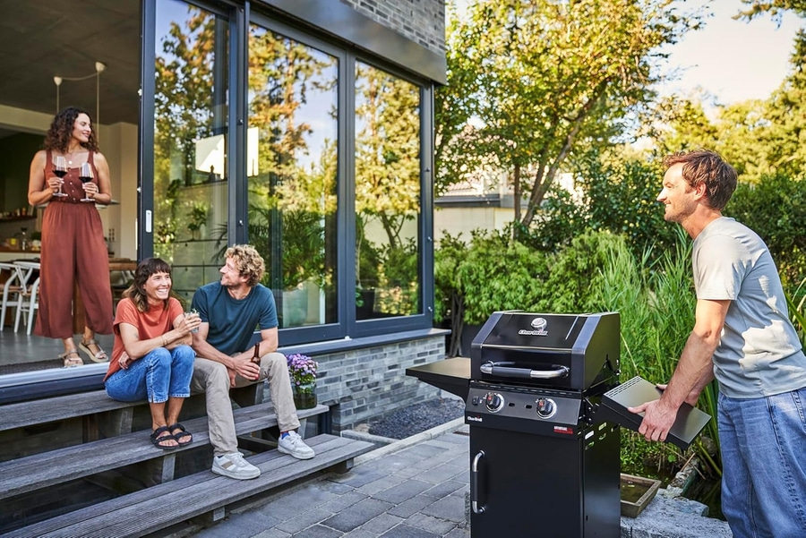 Freunde grillen im Garten. Mann öffnet Grill. Frau mit Wein.