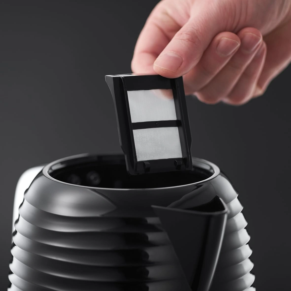 Hand hält Filter über schwarzem Wasserkocher, Nahaufnahme, Detailaufnahme, Filter wird eingesetzt