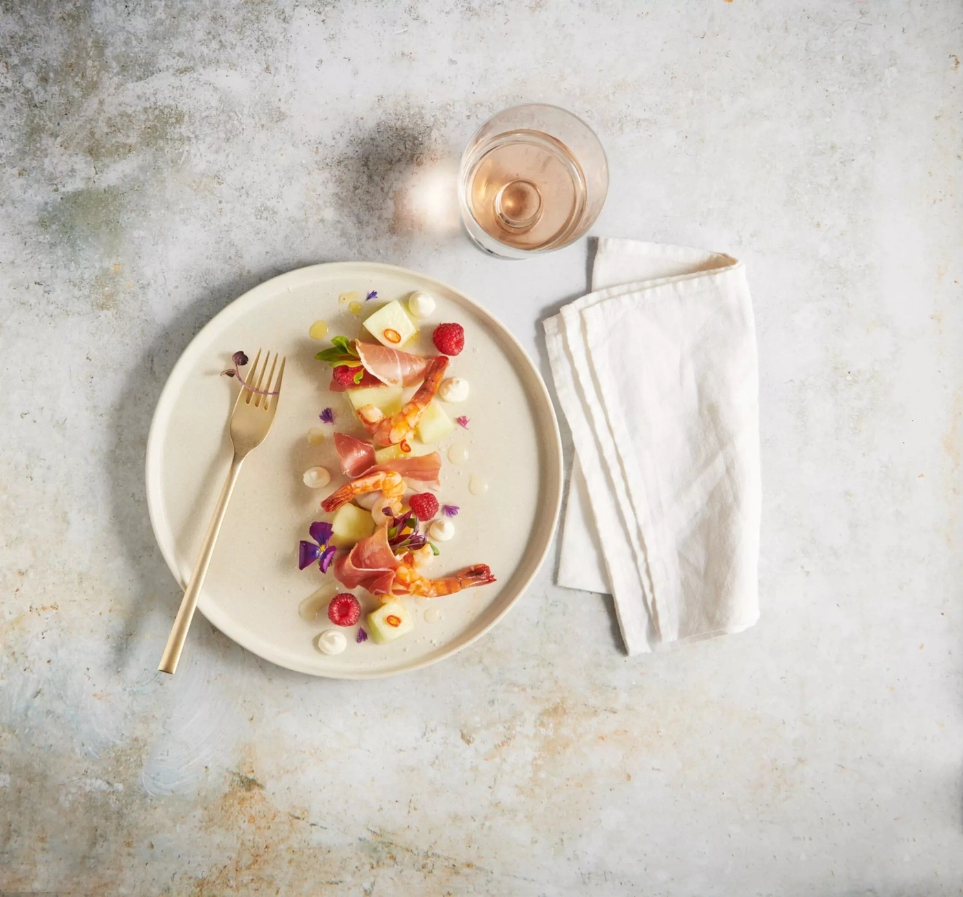 Garnelen mit Melone, Schinken und Beeren auf einem Teller mit Roséwein.
