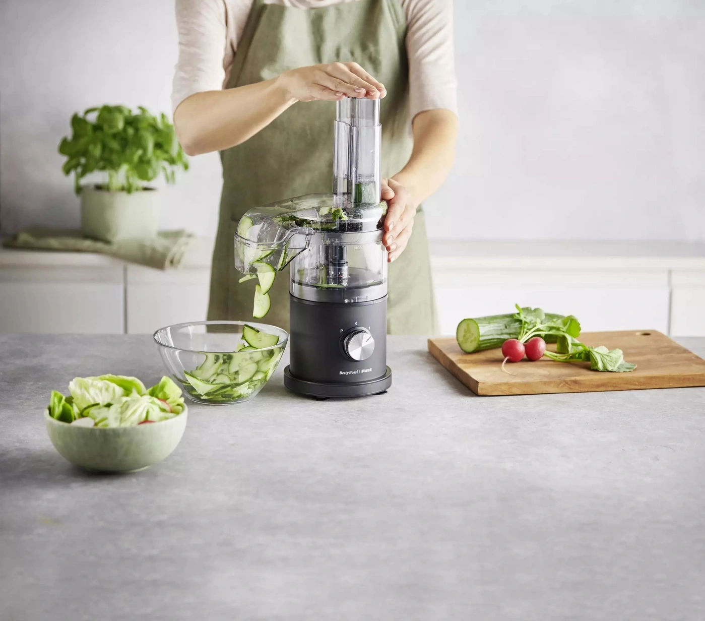 Person schneidet Gurke mit Küchenmaschine, daneben Schüsseln mit Salat und Gemüse