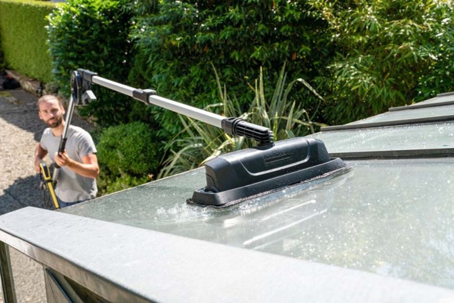 Mann reinigt Glasdach mit einem Reinigungsgerät im Freien.