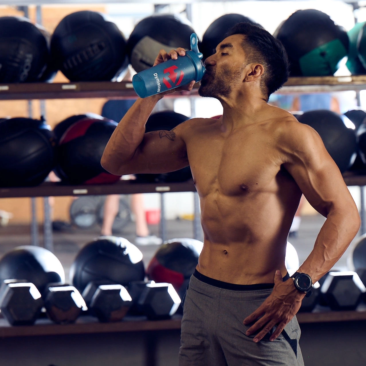 Ein muskulöser Mann trinkt aus einem blauen Shaker im Fitnessstudio.