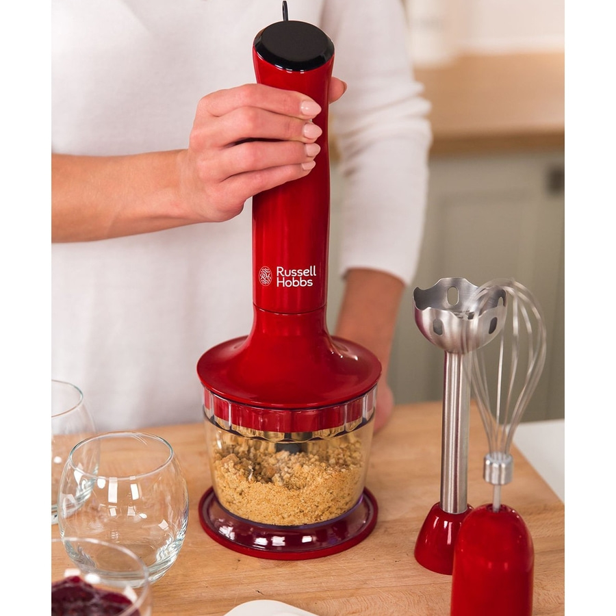 Person hält roten Stabmixer mit Zubehör auf Holzbrett.