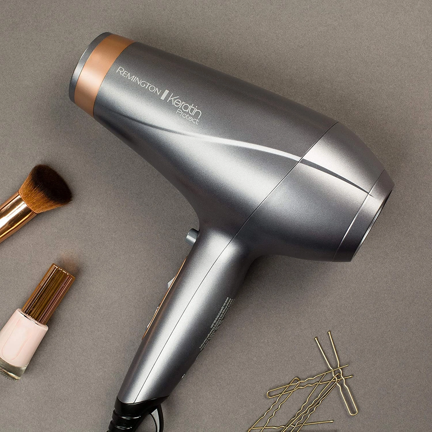Haartrockner, Make-up-Pinsel, Nagellack und Haarnadeln auf grauem Hintergrund.