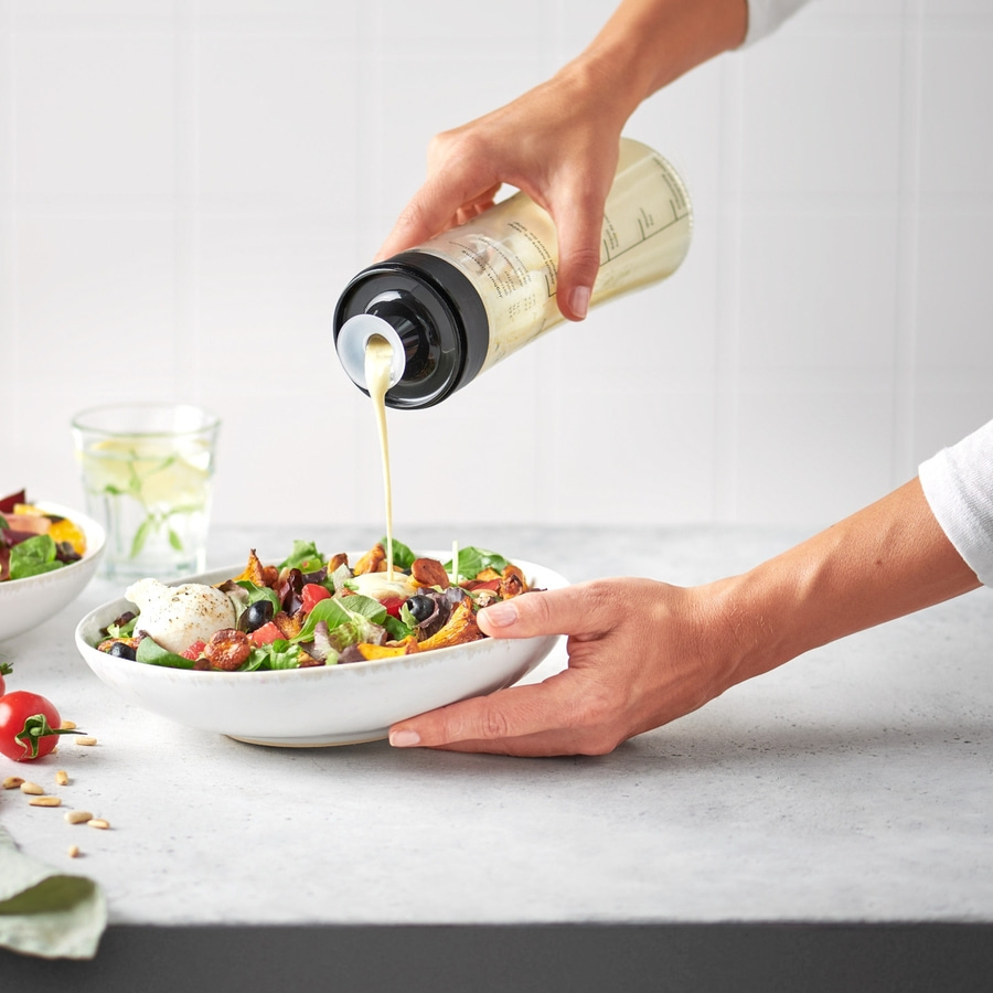 Person gießt Salatdressing über einen Salat in einer Schüssel.