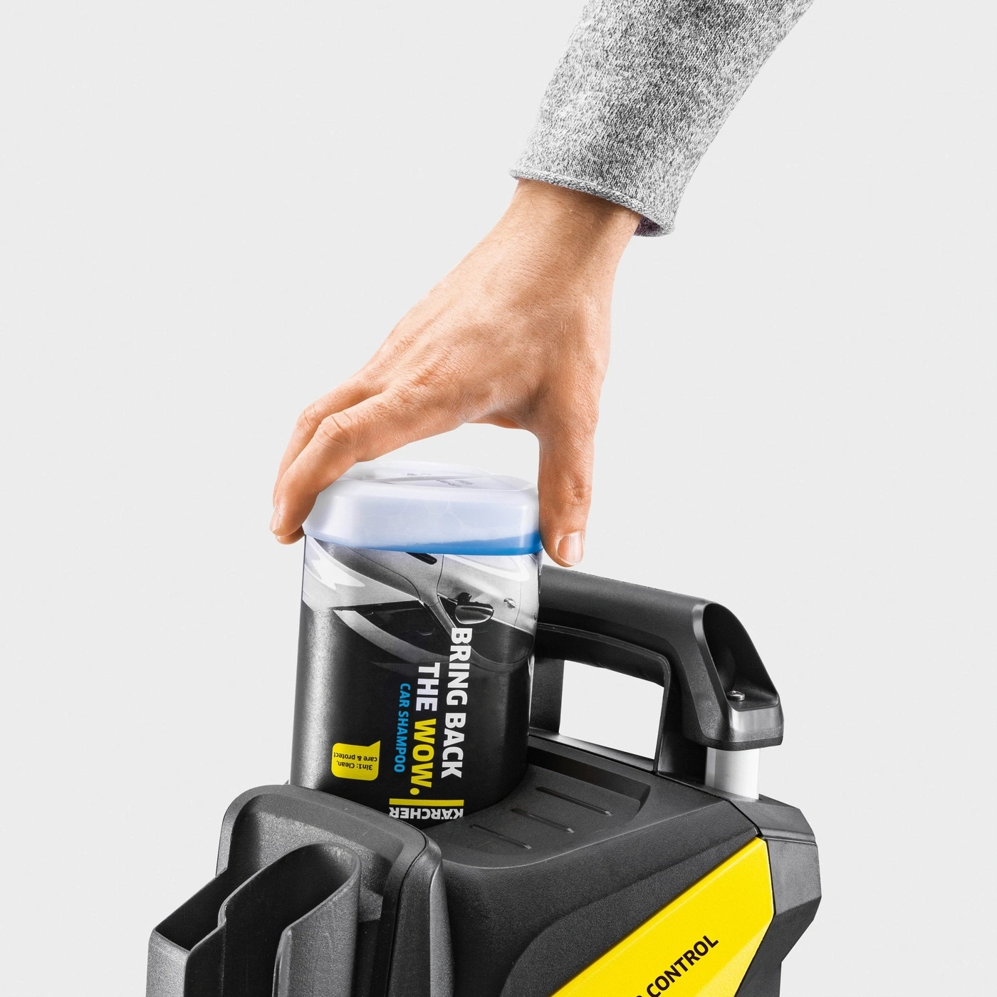 Hand hält Flasche mit Autoshampoo auf Hochdruckreiniger