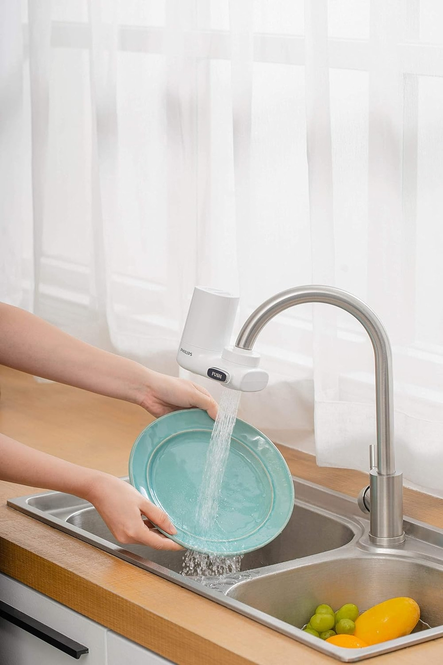 Person wäscht Teller unter fließendem Wasser in der Küche mit Philips Wasserfilter.