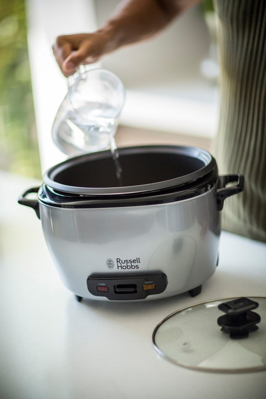 Person gießt Wasser in einen Reiskocher der Marke Russell Hobbs.