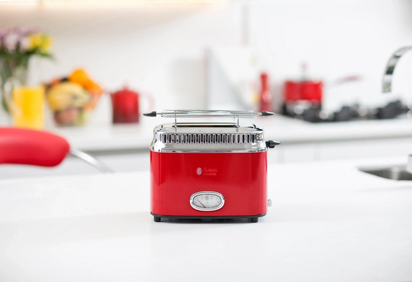 Roter Toaster auf weißer Oberfläche in einer Küche mit Blumen und Obst.